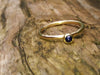 Blue Sapphire Tiny Gold Stacking Ring sitting on a log