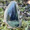 Sterling silver ring with a large green freeform oval Nebula Jasper stone surrounded with tendrils. The ring sits on a bed of moss.