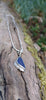 Triangle-ish  deep blue seaglass pendant with tendril detail on smooth slim snake chain on a mossy wooodland log.