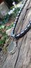 Round-ish olive seaglass pendant with tendril detail on black rice shaped pearls on a mossy wooodland log. 