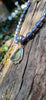 Small triangle-ish mid green seaglass pendant with tendril detail on black freshwater pearl beads draped on a mossy woodland log.