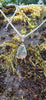Small triangle-ish mid green seaglass pendant with tendril detail on thick spiga chain draped on a mossy rock.
