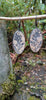 Black silver large drop earrings set with rough sandy coloured stone with black seaweed like inclusions, hang from a twig in the forest.
