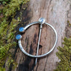 Traditional Silver brooch, penannular pin, ring pin with blue stones on a mossy log.