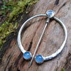 Traditional Silver brooch, penannular pin, ring pin with blue stones on a mossy log.