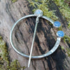Traditional Silver brooch, penannular pin, ring pin with blue stones on a mossy log.