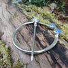 Traditional Silver brooch, penannular pin, ring pin with blue stones on a mossy log.