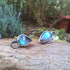 Bud shaped with tendril tails oxidised silver stud earrings with a dreamy elfin quality sits on a mossy log, the labradorite stones glinting blue in the sunlight.
