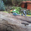 Leaf shaped oxidised silver stud earrings with a dreamy elfin quality sits on a mossy log, the labradorite stones glinting blue in the sunlight.