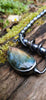 Bud shaped labradorite pendant with a tendril  curling around the string of black lustrous freshwater pearls. With a dreamy elfin it quality sits on a mossy log, the labradorite stone glinting blue and orange in the sunlight.