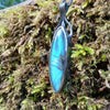Large oval Labradorite and oxidised sterling silver pendant and long thick chain sitting on a mossy log, the labradorite stone bud is clasped by black tendrils  and glints blue in the sunlight.