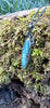 Large oval Labradorite and oxidised sterling silver pendant and long thick chain sitting on a mossy log, the labradorite stone bud is clasped by black tendrils  and glints blue in the sunlight.
