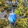Large Bud shaped Labradorite and oxidised sterling silver pendant sitting on a mossy rock, the labradorite stone bud grows out of a tangle of tendrils winding their way around a thick chain and glints blue in the sunlight.