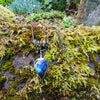 Large Bud shaped Labradorite and oxidised sterling silver pendant sitting on a mossy rock, the labradorite stone bud grows out of a tangle of tendrils winding their way around a thick chain and glints blue in the sunlight.