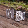 melt textured silver studs sitting on a mossy log in the sunshine.