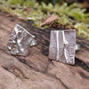 melt textured silver studs sitting on a mossy log in the sunshine.