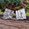 melt textured silver studs sitting on a mossy log in the sunshine.