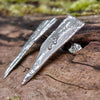 long triangle shaped melt textured silver studs sitting on a mossy log in the sunshine.