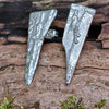 long triangle shaped melt textured silver studs sitting on a mossy log in the sunshine.