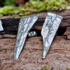 long triangle shaped melt textured silver studs sitting on a mossy log in the sunshine.