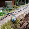 An oxidised silver necklace with a dreamy elfin quality sits on a mossy log in the sunlight.