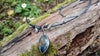 An oxidised silver necklace with a dreamy elfin quality sits on a mossy log in the sunlight.