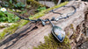 An oxidised silver necklace with a dreamy elfin quality sits on a mossy log in the sunlight. Daisies are growing in the background.