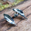 Small oxidised silver 3d leaf stud earrings sitting on an old log in the sunshine.