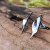 Small oxidised silver 3d leaf stud earrings sitting on an old log in the sunshine.