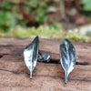 Small oxidised silver 3d leaf stud earrings sitting on an old log in the sunshine.