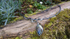 An oxidised silver necklace with a dreamy elfin quality sits on a mossy log in the sunlight.