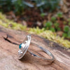 Silver ring with a textured circular top and a small green stone, sitting on a mossy log