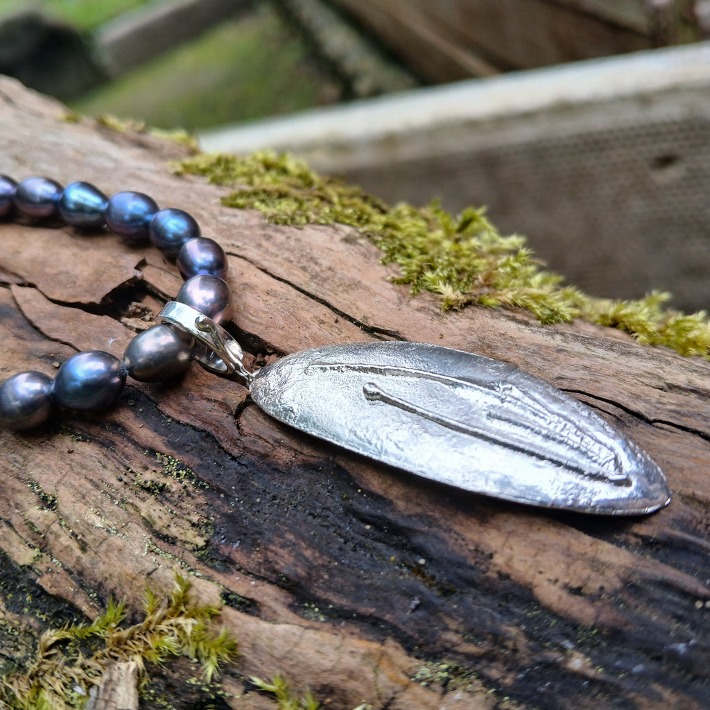 Sterling silver oval melt textured pendant with black oval freshwater pearl beads, lying n a mossy log
