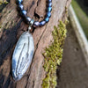 Sterling silver oval melt textured pendant with black oval freshwater pearl beads, lying n a mossy log