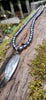 Sterling silver oval melt textured pendant with black oval freshwater pearl beads, lying n a mossy log