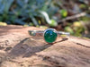 Silver and Green agate stacking ring Sitting on a mossy Woodland log in the sunlight.