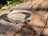 Silver and Peridot stacking ring Sitting on a mossy Woodland log in the sunlight.