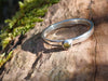 Silver and Peridot stacking ring Sitting on a mossy Woodland log in the sunlight.