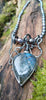 Black oxidised sterling tangle of tendrils wrap around a string of oval shaped black freshwater pearls, terminating in a large bud shaped labradorite with a strong blue flash. The necklace sits on a mossy log.