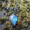 Black oxidised sterling tangle of tendrils wrap around a chunky oxidised silver chain, terminating in a large bud shaped labradorite with a strong blue flash. The necklace sits on a mossy stone.