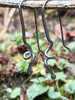 Black oxidised sterling sliver spiral tendril earrings on a twig in the forest.