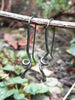Black oxidised sterling sliver spiral tendril earrings on a twig in the forest.