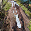 Short sterling silver melt textured pendant on silver chain. The necklace lies on a mossy log.
