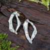 Sterling silver Femscape earrings sitting on a mossy log.
