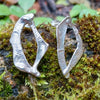 Sterling silver Femscape earrings sitting on a mossy log.