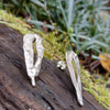 Sterling silver Femscape earrings sitting on a mossy log.