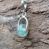 Silver pendant with a semi transparent pale blue green bead on a log. 