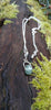 Silver pendant with a semi transparent pale blue green bead on a log. Showing fine chain with extender.