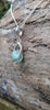 Silver pendant with a semi transparent pale blue green bead on a log. 