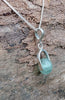 Silver pendant with a semi transparent pale blue green bead on a log. 
